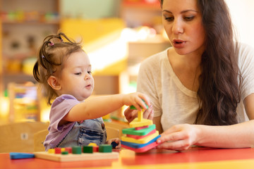 Fototapeta na wymiar Teacher and kid girl playing colorful block toys in creche