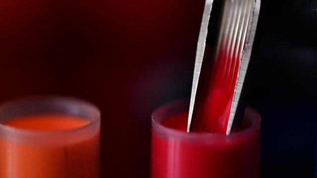 Extreme closeup of tattoo needle dipping in cap filled with red tattoo ink - needle moving out of  frame - slow motion footage