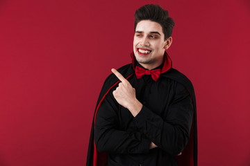 Image of vampire man in black halloween costume pointing finger - obrazy, fototapety, plakaty