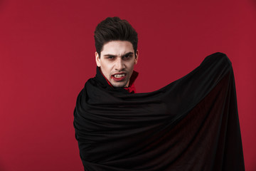 Image of vampire man in black halloween costume holding his cloak - obrazy, fototapety, plakaty