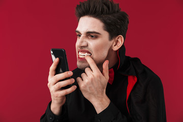 Image of vampire man in black halloween costume holding smartphone