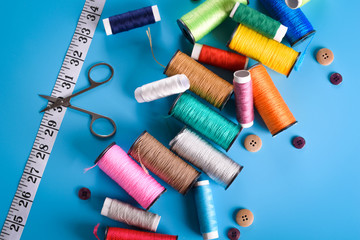 Sewing kit: scissors, measuring tape, thimbles, threads and buttons. Composition with threads and accessories on blue background Colored coils on blue background, place for text