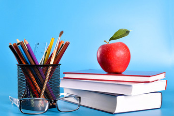  School supplies pencils, pens, ruler, brush , books and apple on a blue background with a place for text