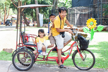 Fototapeta na wymiar Happy family in holiday, Father riding a tricycle for his son and daughter to sit.