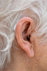 Hearing aid. Female pensioner with white hair wearing a Behind The Ear, BTE, hearing aid. Close up of ear. Vertical.