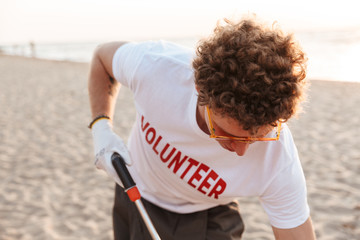 Image of male caucasian volunteer cleaning beach and picking up trash