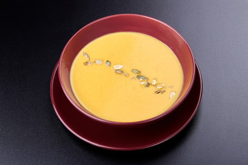 Pumpkin cream soup with pumpkin seeds in a black bowl. Grey stone background. Top view
