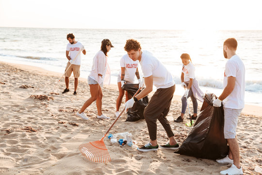 Image of young voluntary workers cleaning beach from plastic at seashore