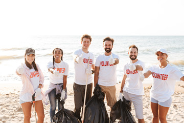 Photo of eco volunteers showing thumbs up while cleaning beach from trash