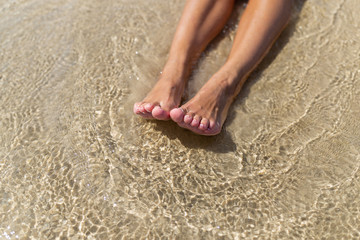 Top view of naked tanned female feet in the sand on the beach, point of view of feet in the sand with sea foam ocean summer background-image, relaxing on the ocean beach, feet on the sea sand-image