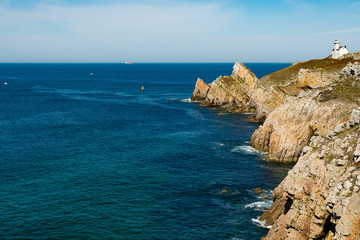 jagged rocky coastline with deep blue ocean and a white lighthouse