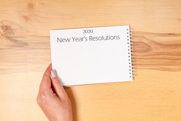 Obraz premium New year Concept - 2020 number and text on notepad and female hands of copy background. top view