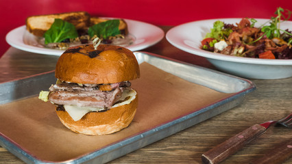 Close-up of traditional American beef burger with cheese served on pieces of brown paper, salad on the background, front view.