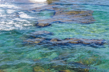 a wave runs over the rocky shore. clear turquoise water