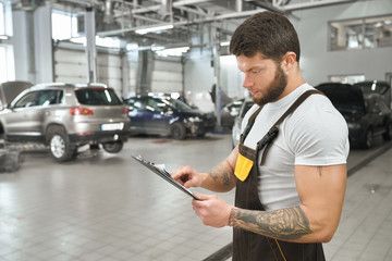 Muscular mechanic in coveralls reading from folder.