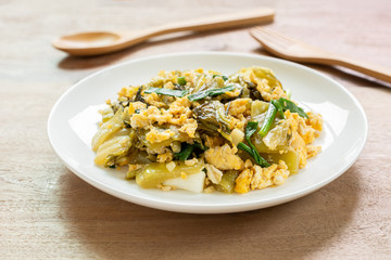 close up of stir fried pickled mustard green with egg in a ceramic dish on wooden table. asian homemade style food concept.