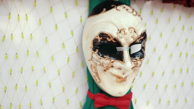 carnival, on wall hangs a white mask with black eyes, Golden lips and patterns and red butterfly around his neck, close-up, slow motion