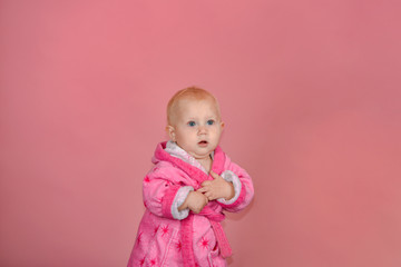 Little girl in a pink bathrobe on a pink background in the studio.
