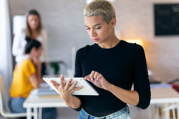 Concentrated young entrepreneur woman using her digital tablet while standing in the office.