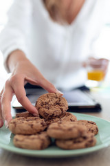 A woman's hand taking chocolate cookies from a plate while holding an orange juice in the other hand.