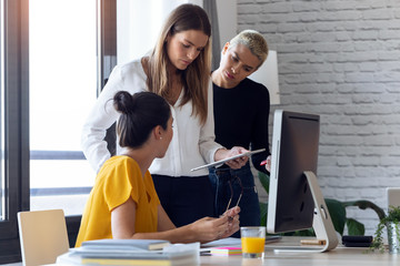 Three modern businesswomen talking and reviewing the latest work done on the digital tablet in a...