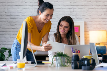 Two young businesswomen talking and reviewing they last work in the digital tablet in the office.