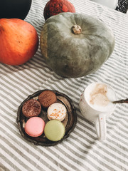 Pumpkins, hot coffee and macaroons on vintage plate on rustic table. Autumn morning. Fall decor on rustic table