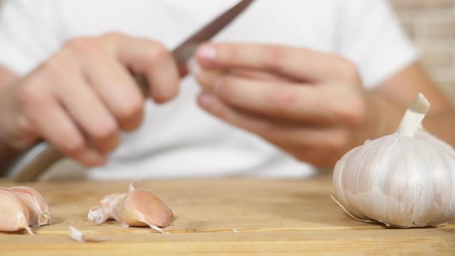 closeup head of garlic, male hands peel the garlic on a wooden board