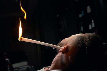 Close up of man's head with burning stick in ear at salon