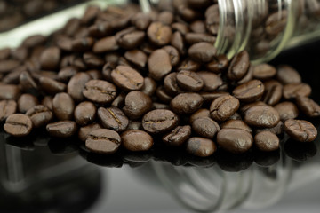 Roasted coffee beans from bottle glass spread on black table with reflection