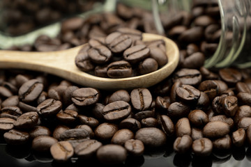 Roasted coffee beans in wooden spoon and spread on black table with bottle glass
