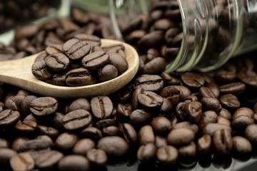 Roasted coffee beans in wooden spoon and spread on black table with bottle glass