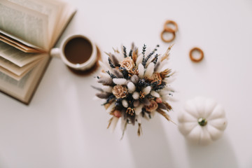 Top view of workspace or office desk. Cup of coffee, book and dried flowers at white background. Flat lay, top view
