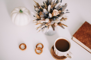 Top view of workspace or office desk. Cup of coffee, book and dried flowers at white background. Flat lay, top view