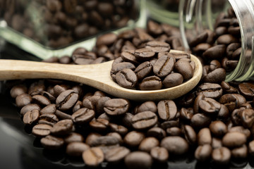 Fototapeta premium Roasted coffee beans in wooden spoon and spread on black table with bottle glass