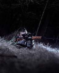 armed man in camouflage clothes in the forest with a sniper rifle aims at the sniper scope