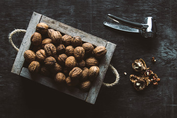 Box with tasty walnuts and nutcracker on dark wooden table, closeup