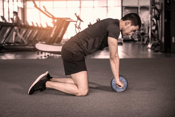 Athlete sporty man doing exercise with abs roller wheel to strengthen his abdominal muscle in gym.