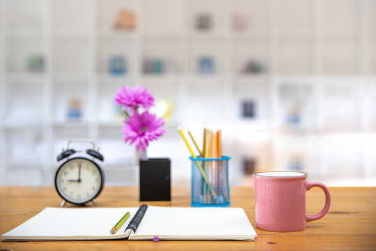 office table desk. Workspace with pink coffee cup , blank note book, alarm colck and office supplies background.