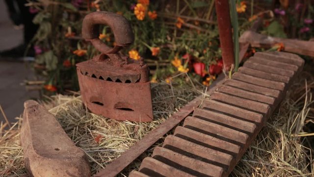 very old tools for everyday life, rusty iron, washboard, rusty sword, lying on table with hay, in background of small flowers, close-up, slow motion