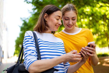 smiling mother and daughter looking art cellphone in park