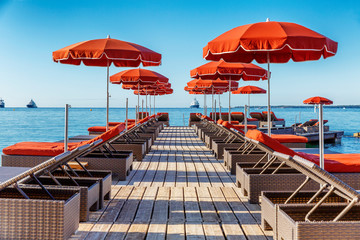 A row of deck chairs with orange mattresses and umbrellas in a fashionable resort. A clear sunny day.