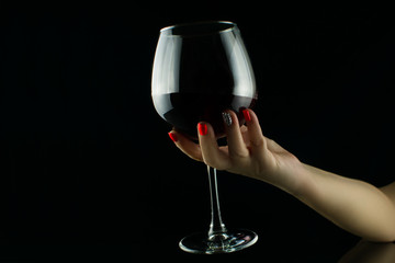 Female hand holding glass of wine on black background