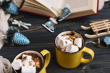 Mugs with marshmallows near Christmas decorations and book