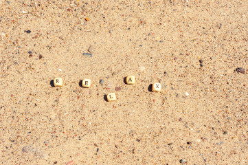 The letters on the wooden cubes are folded into the word RELAX on the sand