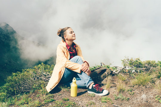 Young white hipster woman high in the mountains against the background of clouds resting and enjoying the natural beauty. Copy space for text.