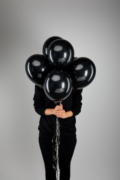Woman with obscure face holding bunch of black balloons isolated on grey, black Friday concept
