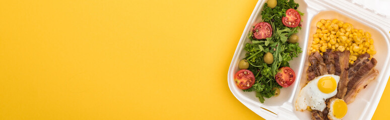 panoramic shot of eco package with corn, meat, fried eggs and salad isolated on yellow