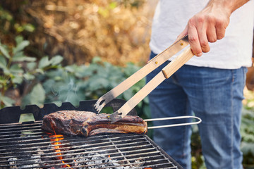 Fototapeta premium cropped view of man with tweezers grilling meat on barbecue grid