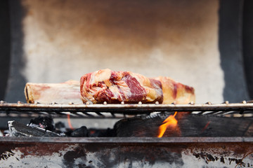 raw meat grilling on barbecue grid and coal pieces outside